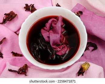 Bowl of hibiscus flower   broth   and dried sepals of the hibiscus are on the samples of cotton fabric in gradient purple color, background. Natural dyeing for fabrics, DIY
 - Shutterstock ID 2258471871