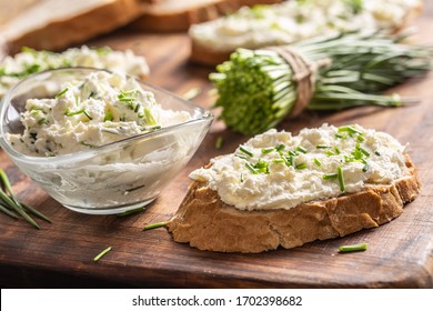A bowl of homemade cream cheese spread with chopped chives surrounded by bread slices with spread and a bunch of freshly cut chives.