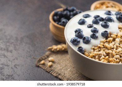 Bowl of homemade crispy granola with yogurt, fresh blueberry and wheat seeds on a stone background. healthy cereal morning breakfast.
