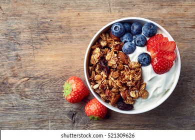 Чаша самодельной гранолы с йогуртом и свежими ягодами на деревянном фоне с видом сверху