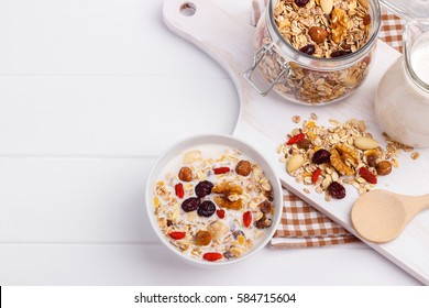 Bowl of homemade muesli with nuts, berries, dried fruits, milk and honey on white wooden background. Healthy breakfast. top view