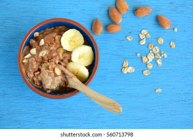 Bowl Of Homemade Oatmeal Spelt Porridge With Banana, Almonds And Almond Butter, On Blue Background