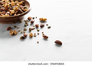 A Bowl Of Homemade Trail Mix With Some Of The Mix Scattered In Front, Taken From Above, Against A White Background.