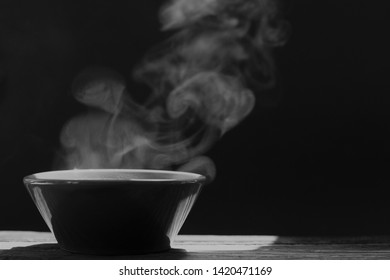 Bowl Of Hot Soup With Steaming On Wooden Table On Black Background