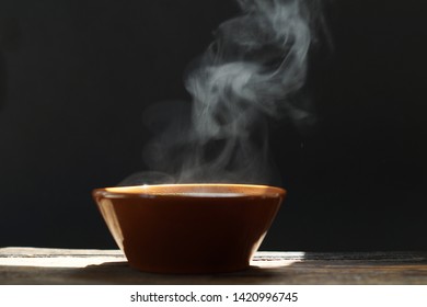 bowl of hot soup with steaming on wooden table on black background