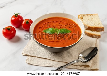 Bowl of hot tomato soup over marble background. Hot vegetable soup puree, spoon and bread. Healthy vegetarian dish of roasted tomatoes with garlic and basil. Mediterranean cuisine. Top view.