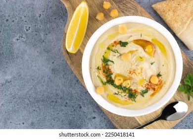 Tazón de humus con garbanzos, paprika, perejil y aceite de oliva sobre fondo gris, vista superior. Hummus con limón y pita