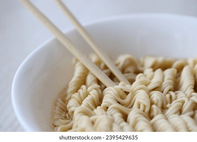 Bowl of instant cooking noodles with wooden chopsticks on white wooden table close up - Shutterstock ID 2395429635