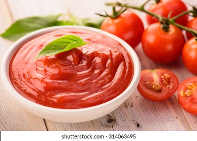 bowl of ketchup or tomato sauce and fresh tomatoes on wood table