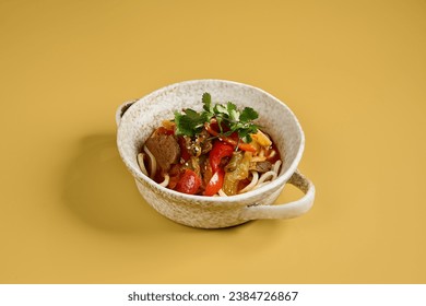 A bowl of Lagman, a traditional Asian noodle dish, featuring stir-fried beef and vegetables such as bell peppers, onions, and carrots, garnished with herbs and served in a rustic ceramic bowl. - Powered by Shutterstock