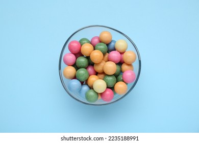 Bowl with many bright gumballs on light blue background, top view