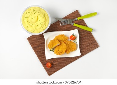 bowl of mashed potato puree with chopped chives and plate of breaded turkey breast on brown place mat