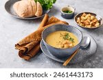 Bowl of mashed potato soup with a spoon on the plate. The bowl is filled with yellow soup puree and topped with croutons, parsley and ground red pepper.