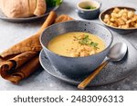 Bowl of mashed potato soup with a spoon on the plate. The bowl is filled with yellow soup puree and topped with croutons, parsley and ground red pepper.