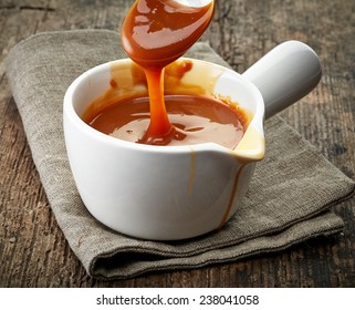 Bowl Of Melted Caramel Sauce On Old Wooden Table