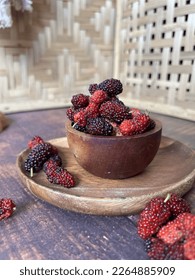 A bowl of mulberry on wooden plate, some mulberry is placed here and there, with traditional look background