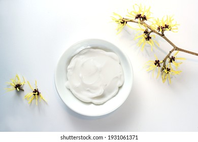 Bowl With Natural Cosmetics Creme And Yellow Blooming Witch Hazel (Hamamelis), Medical Plant For Skin Care And Alternative Medicine, Light Gray Background, Copy Space, High Angle View From Above