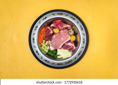 Bowl Of Natural Raw Dog Food On Yellow Background. BARF Dog Diet. Fresh Meat, Eggs, Vegetables Close Up