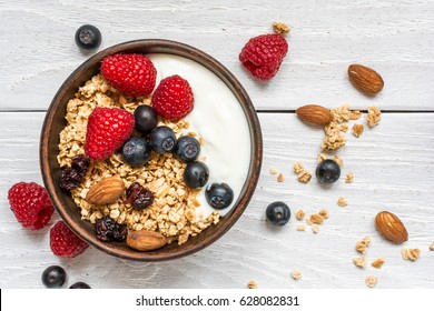 bowl of oat granola with yogurt, fresh raspberries, blueberries and nuts on white wooden board for healthy breakfast. top view - Shutterstock ID 628082831
