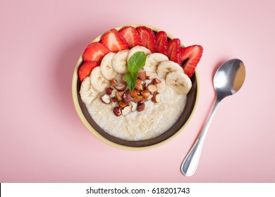 Bowl Of Oatmeal With A Banana, Strawberries, Almonds, Hazelnuts And Butter On A Pink Background. Hot And A Healthy Dish For Breakfast, Top View.
