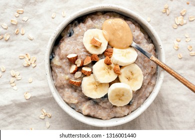 Bowl of oatmeal porridge with banana and peanut butter over linen background. Top view. Healthy vegan breakfast - Powered by Shutterstock