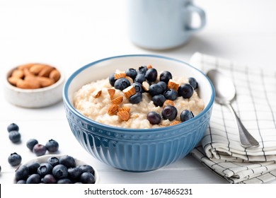 Bowl of oatmeal porridge with blueberries and almond nuts on white table. Healthy breakfast food, clean eating concept