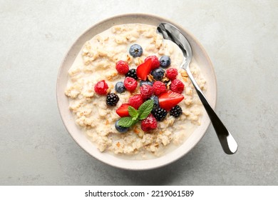 Bowl of oatmeal porridge served with berries on light grey table, top view