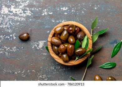 Bowl of olives an olive tree branch, dark background, top view copy space.