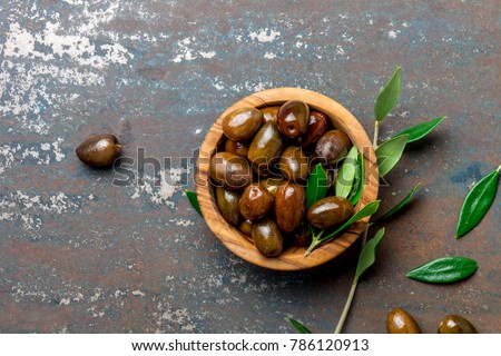 Bowl of olives an olive tree branch, dark background, top view copy space.
