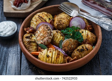 Bowl of oven roasted hassleback Potato with garlic, carrots and onion on rustic black wooden surface