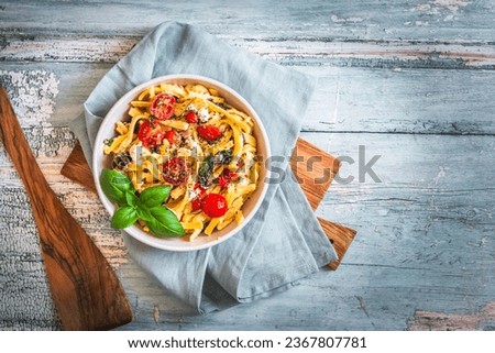Bowl of pasta, noodles, swabian spaetzle, with spinach and cherry tomatoes on rustic wooden table, top view