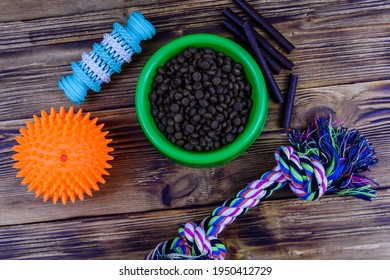 Bowl with pet food, dog toy for teeth cleaning, rope with tied knots and toy ball on wooden background. Top view