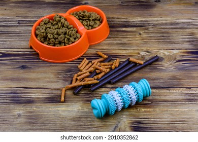 Bowl with pet food, dog toy  for teeth cleaning and dog treats on wooden background