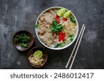 A Bowl Pho Bo traditional Soup with beef, rice noodles, ginger, lime, chili pepper in bowl. Close up. Vietnamese cuisine served on black background