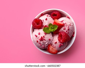 Bowl of pink strawberry ice cream and fresh berries isolated on pink background. Top view