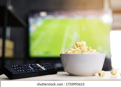 A Bowl Of Popcorn And Remote Control For TV Watching Live Football At Home In The Living Room Relax. Leisure And Entertainment Concept, Copy Space For Text.