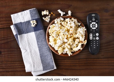 A Bowl Of Popcorn, Towel And A TV Remote On A Rustic Wood Table 