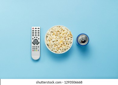 A Bowl Of Popcorn, A TV Remote, A Can With A Drink On A Blue Background. The Concept Of Watching TV, Film, TV Series, Sports, Shows. Flat Lay, Top View.