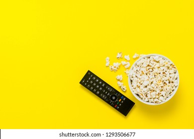 A Bowl Of Popcorn And TV Remote On A Yellow Background. The Concept Of Watching TV, Film, TV Series, Sports, Shows. Flat Lay, Top View.