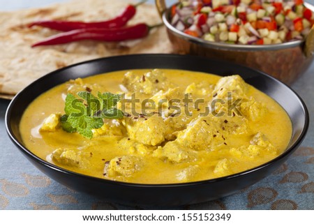 Bowl of pork curry in a creamy sauce flavoured with garlic, cinnamon, coriander, cumin, turmeric and chilli, served with kachumber Indian salad and naan bread. Could be chicken.