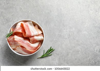 Bowl with raw bacon rashers on grey background