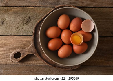 Bowl with raw chicken eggs on wooden table, top view