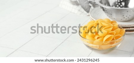 Bowl with raw conchiglie pasta on light tile background with space for text