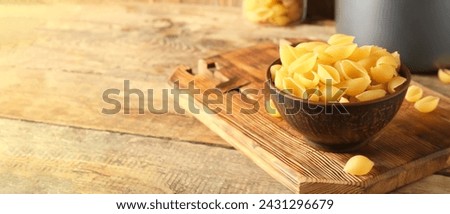 Bowl with raw conchiglie pasta on wooden background with space for text