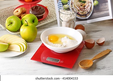 Bowl of raw egg and flour with digital kitchen scales on light wooden table