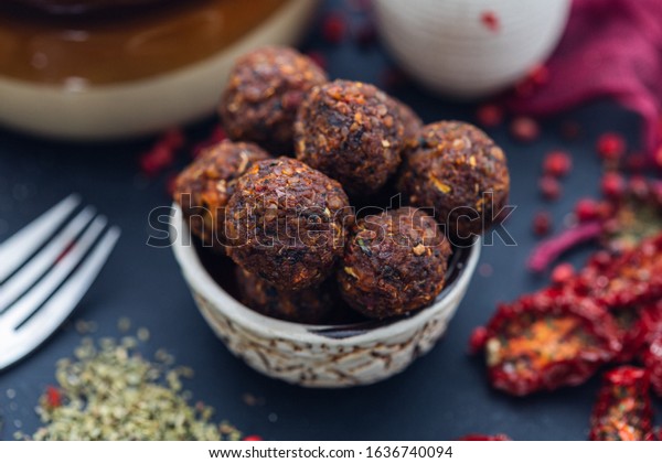Bowl of raw vegan\
meat balls surrounded with vegetables on a dark tabletop flat lay.\
Veggie meatballs. 