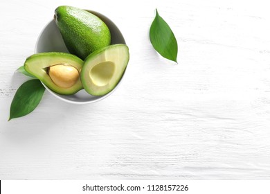 Bowl with ripe avocados on white wooden background