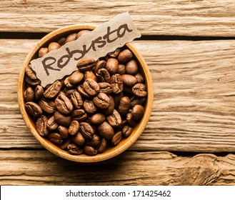 Bowl of Robusta coffee beans over an old wooden table