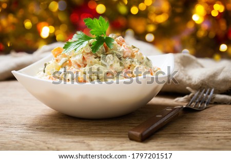 bowl of russian salad olivier with meat and vegetables on a wooden table