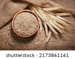 Bowl of rye grains and ears on wooden table, top view